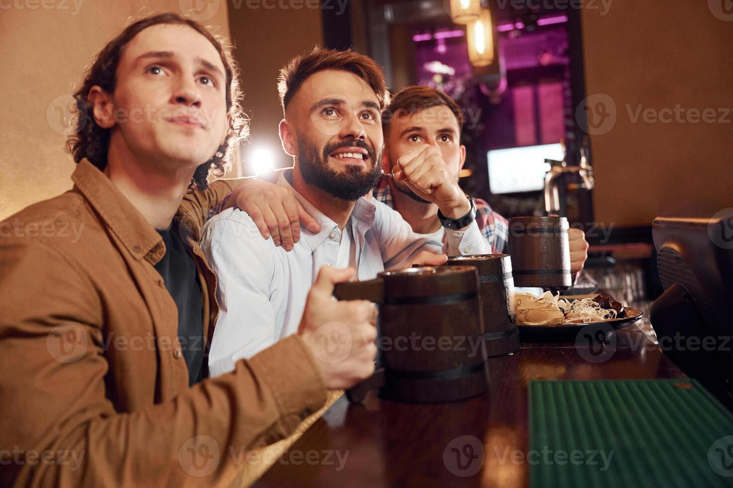 Watching TV.. Three friends are in the bar drinking beer and having a good time photo