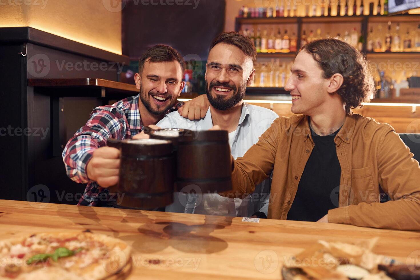 Raising, up the mugs. Three friends are in the bar drinking beer and having a good time photo