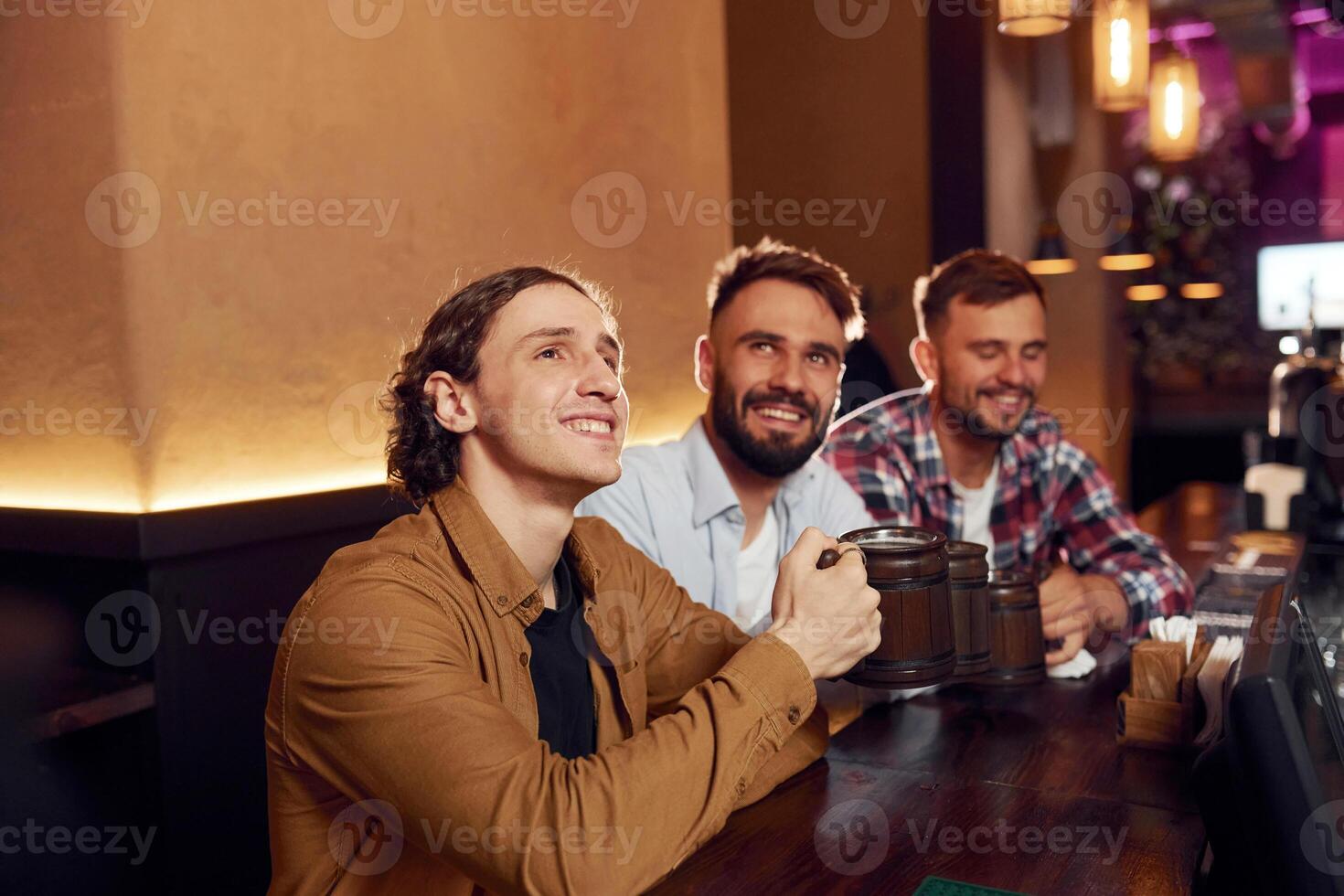 Sitting, and smiling. Three friends are in the, bar drinking beer and having a good time photo