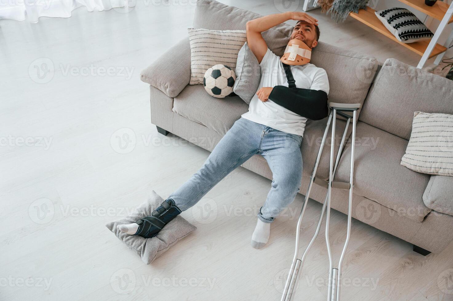 Laying down and suffering from the pain.. Man with crutches is at home indoors. Having injuries photo