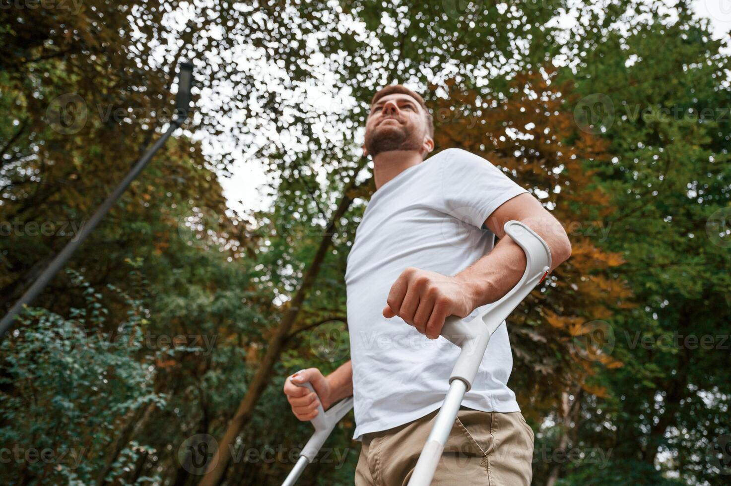 Walking,, view from below. Man with crutches is in the park outdoors. Having leg injury photo