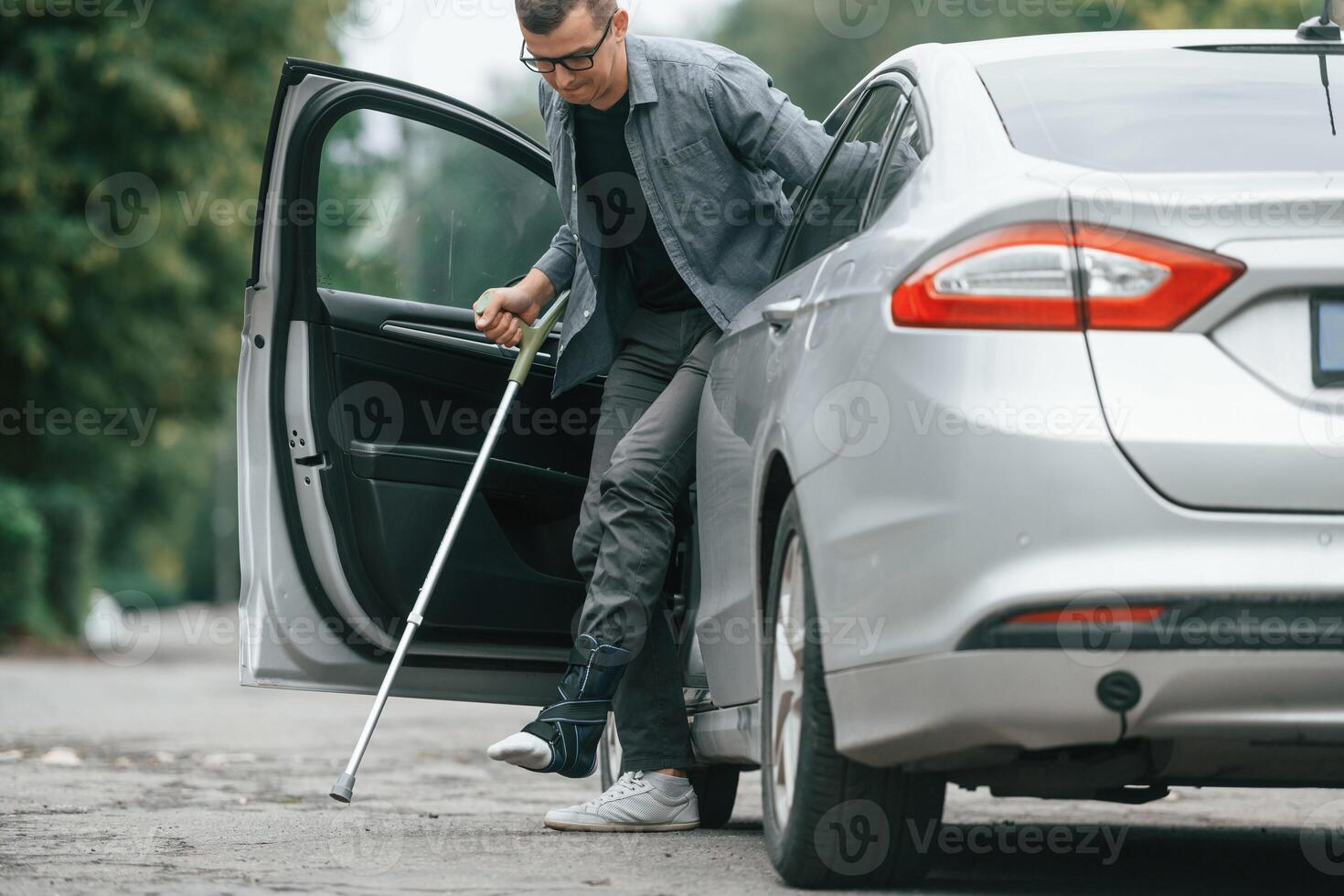 Injured man with crutches is going out from the car.,. photo