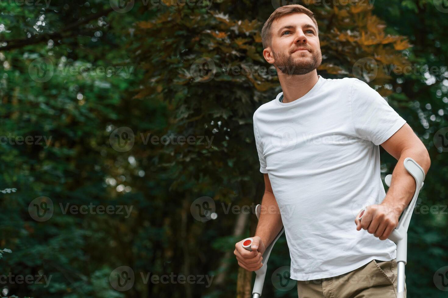 Enjoying the walk. Man with crutches is in the park outdoors. Having leg injury photo