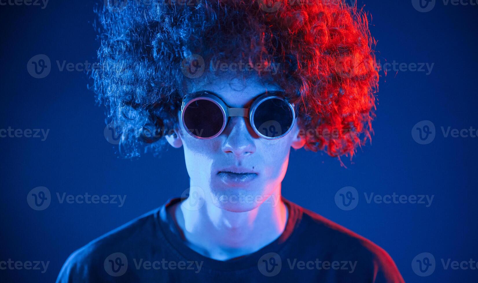Portrait of young man with curly hair that is indoors illuminated by neon lighting. In retro eyewear photo