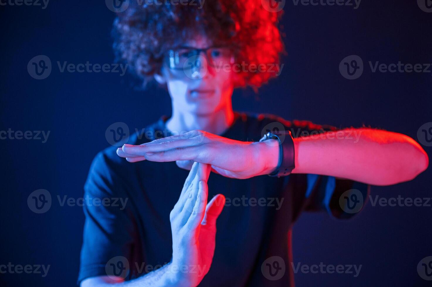 Hands gesture. Young man .with curly hair. is indoors illuminated by neon lighting photo
