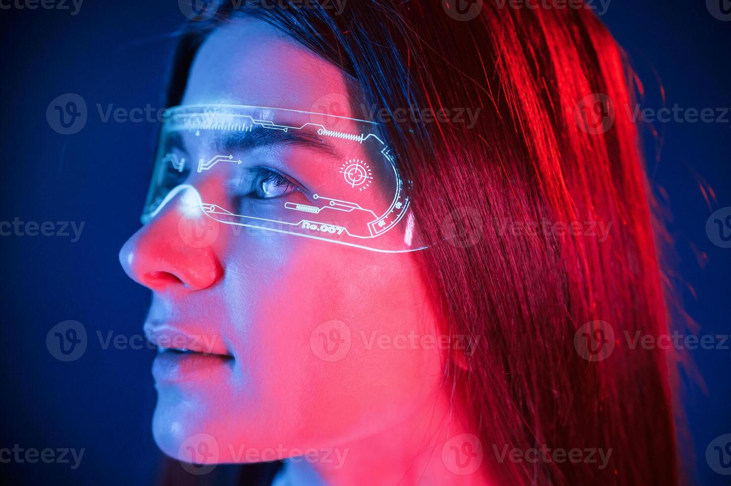 In, futuristic eyewear. Young beautiful woman is indoors in the studio illuminated by neon light photo