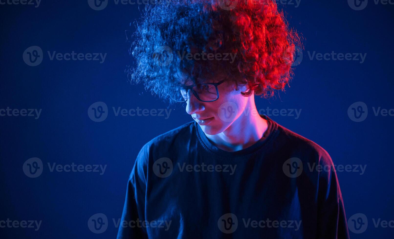 Looking down. Young .man with curly hair is indoors illuminated by neon lighting photo