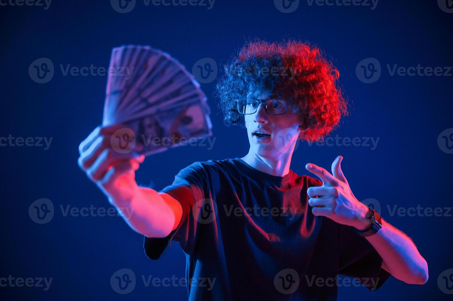 Holding money.,,Young man with .curly hair is indoors illuminated by neon lighting photo