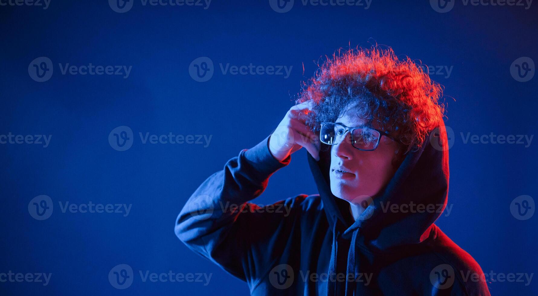 Wearing the hood.. Young man with curly hair is indoors illuminated by neon lighting photo