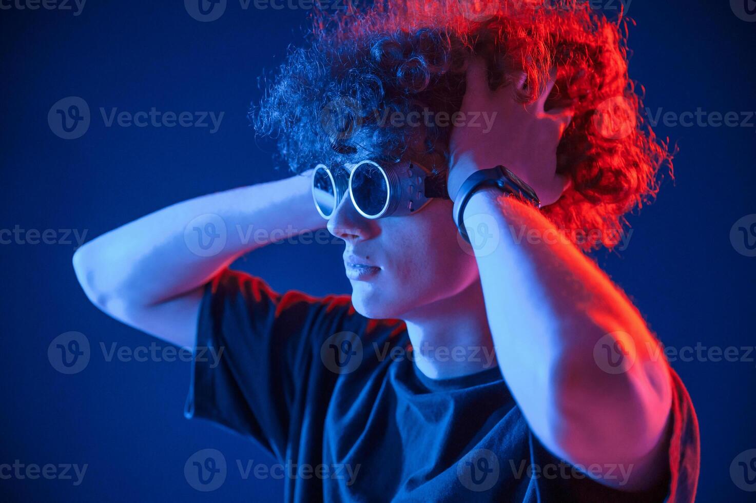 Vintage style glasses.. Young man with curly hair is indoors illuminated by neon lighting photo