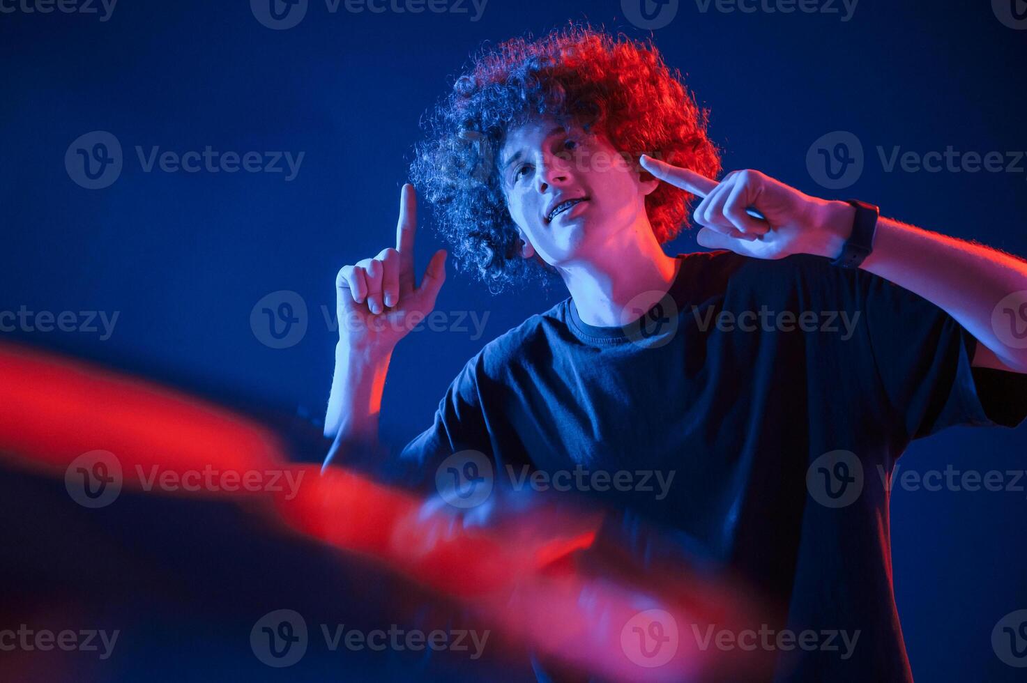 Dj is playing ,music from vinyl. Young man with curly hair is indoors illuminated by neon lighting photo