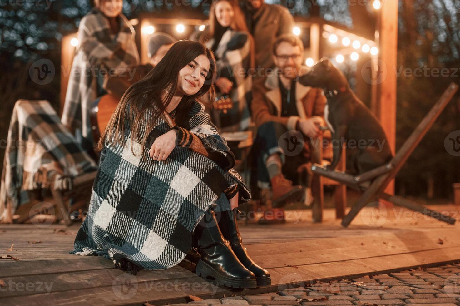 Portrait ,is sitting in front of her friends. Group of people is spending time together on the backyard at evening time photo