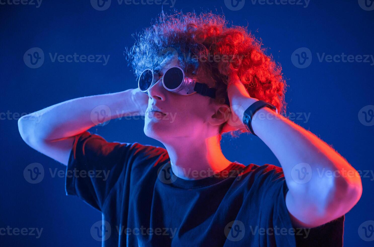 Looking through, the retro glasses. Young man with curly hair is indoors illuminated by neon lighting photo