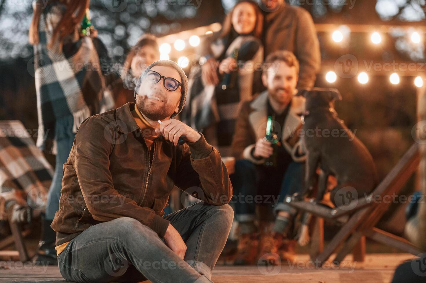 Man is smoking. .Group of people i,s spending time together on the backyard at evening time photo