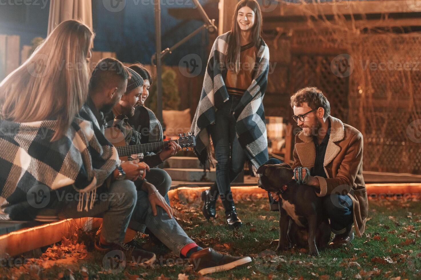 Man is petting, his dog.. Group of people is spending time together on the backyard at evening time photo