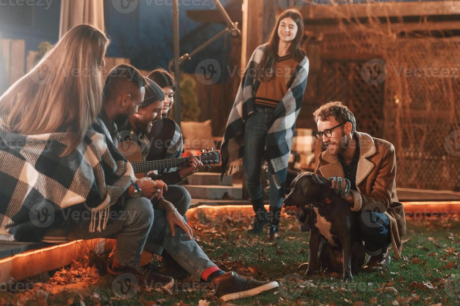 Man is petting, his dog. .Group of people is spending time together on the backyard at evening time photo
