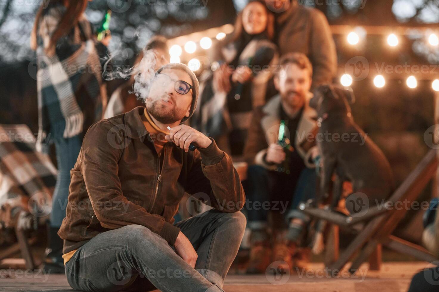 Man is smoking. Group ,of people is spending time together on the backyard at evening time photo