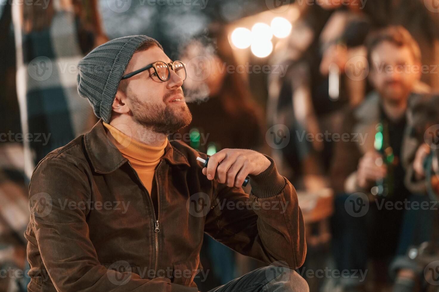 Man is smoking. .Group of people is spending time together on the backyard at evening time photo