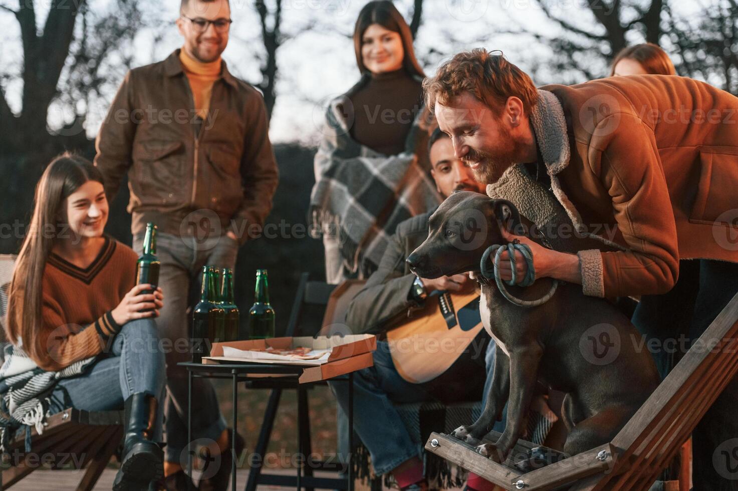 Man is petting his dog. Group of people, is spending time together on the backyard at evening time photo