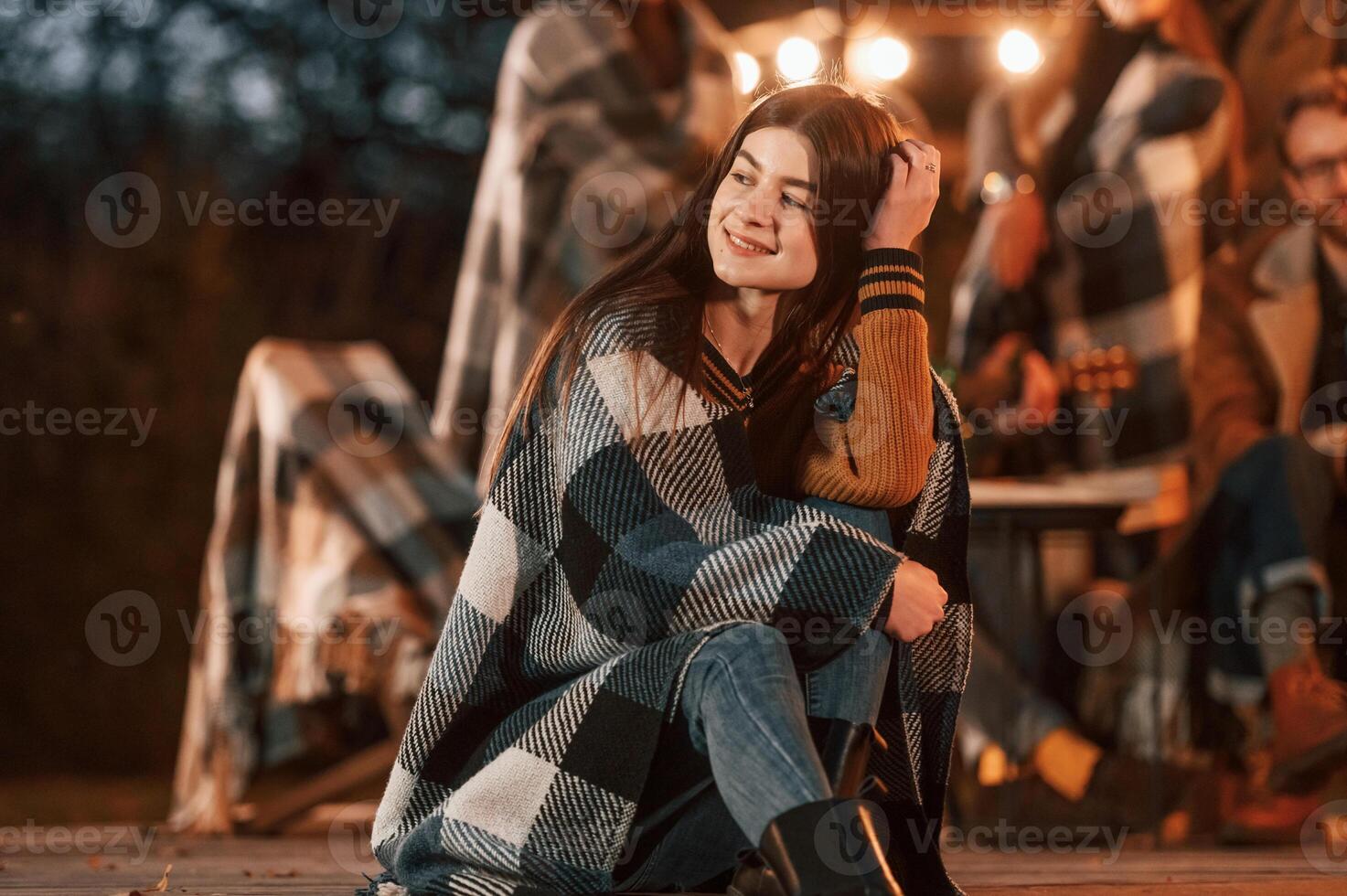 Portrait, is sitting in front of her friends. Group of people is spending time together on the backyard at evening time photo