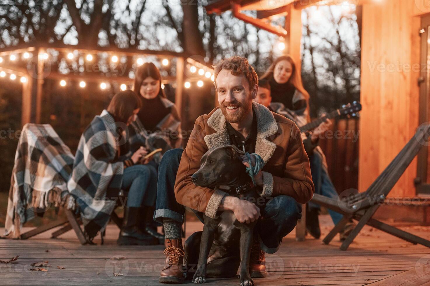 Man is petting his dog. Group of people is spending time together on the backyard at evening time photo