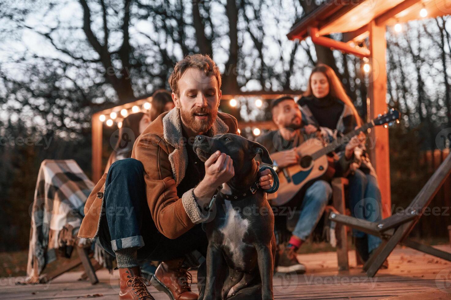 Happy man is sitting with his dog. Group of people is spending time together on the backyard at evening time photo