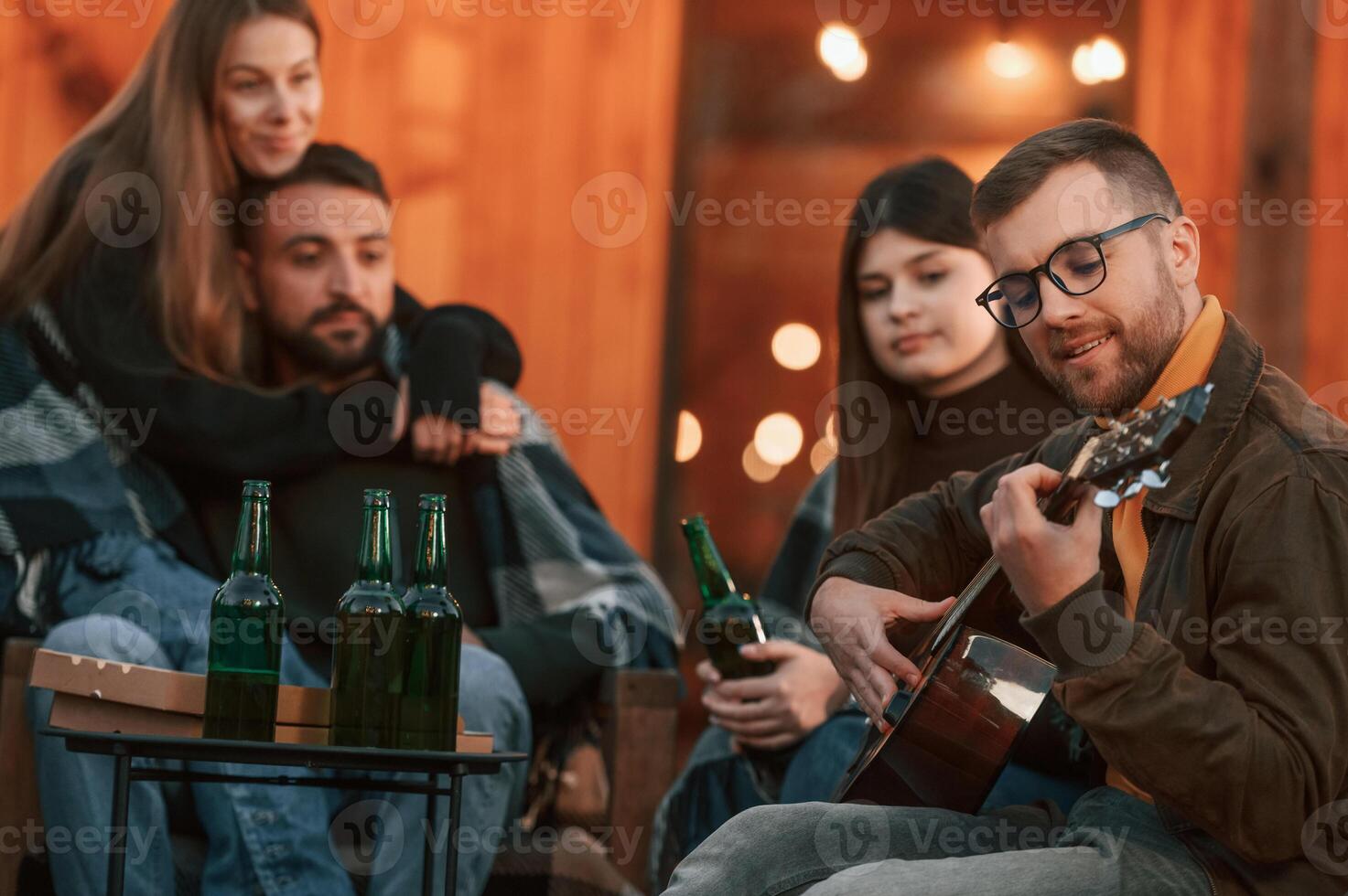 Coneption of weekend. Group of people is, together near beautiful wooden building at evening time photo