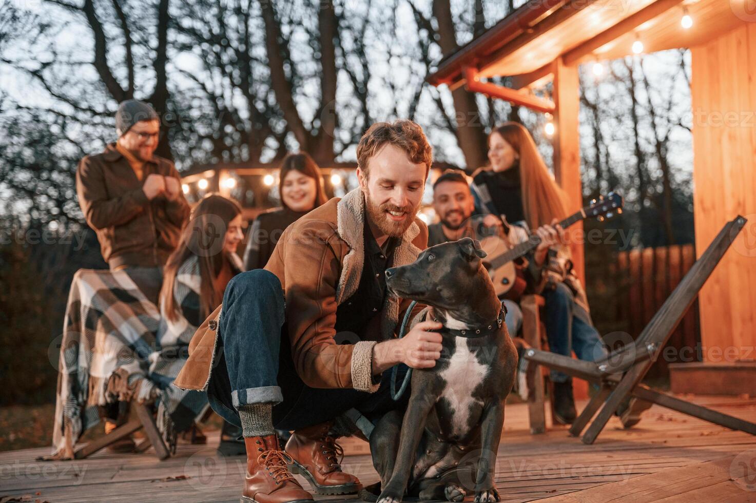 Happy ,man is sitting with his dog. Group of people is spending time together on the backyard at evening time photo