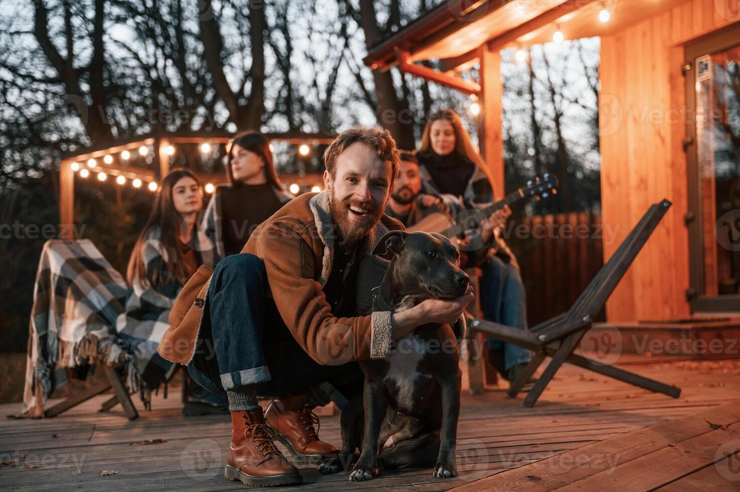 Happy man is sitting with, his dog. Group of people is spending time together on the backyard at evening time photo