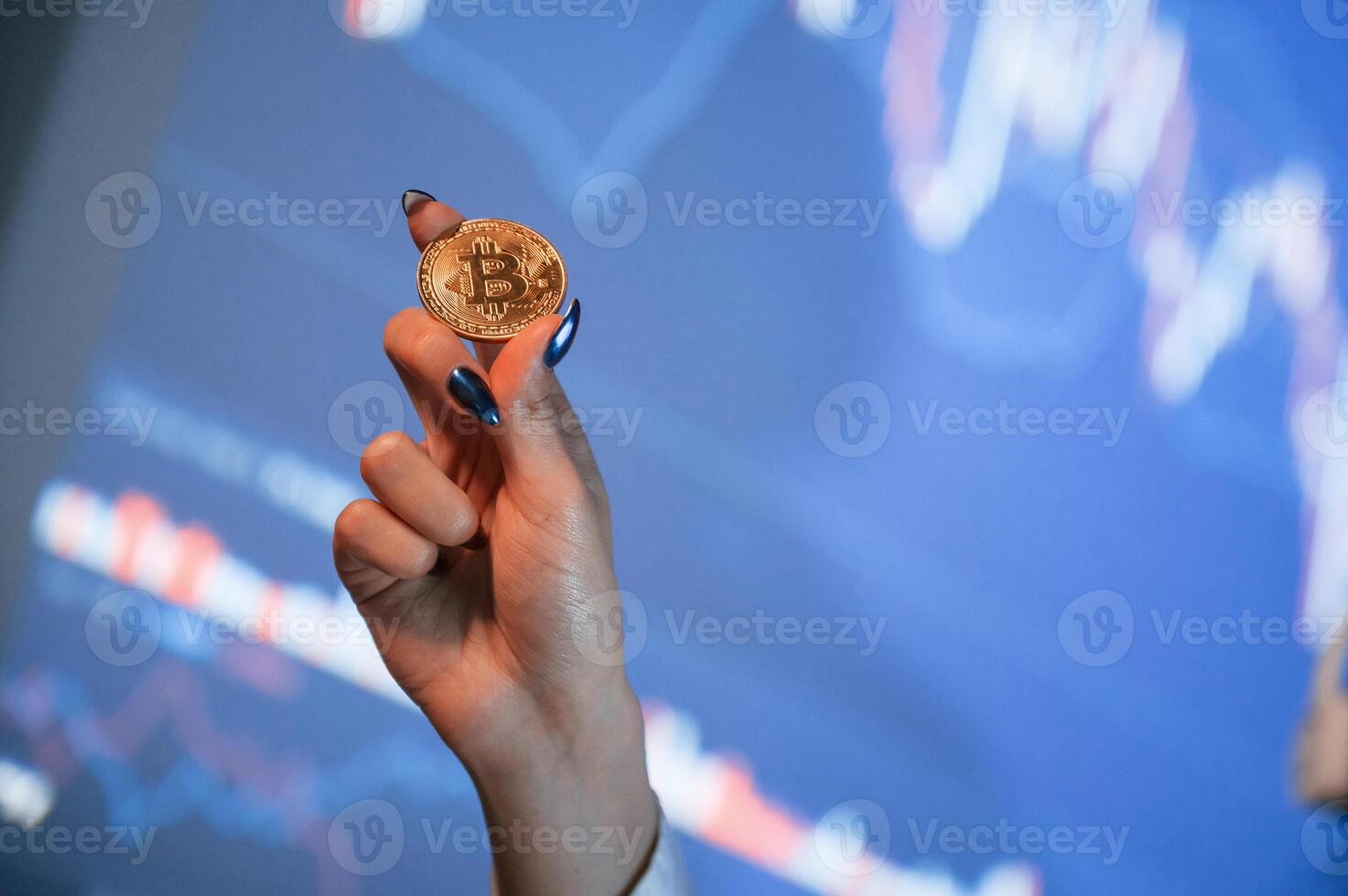 Close up ,view of woman's hand that holding physical bitcoin against background with graphs photo