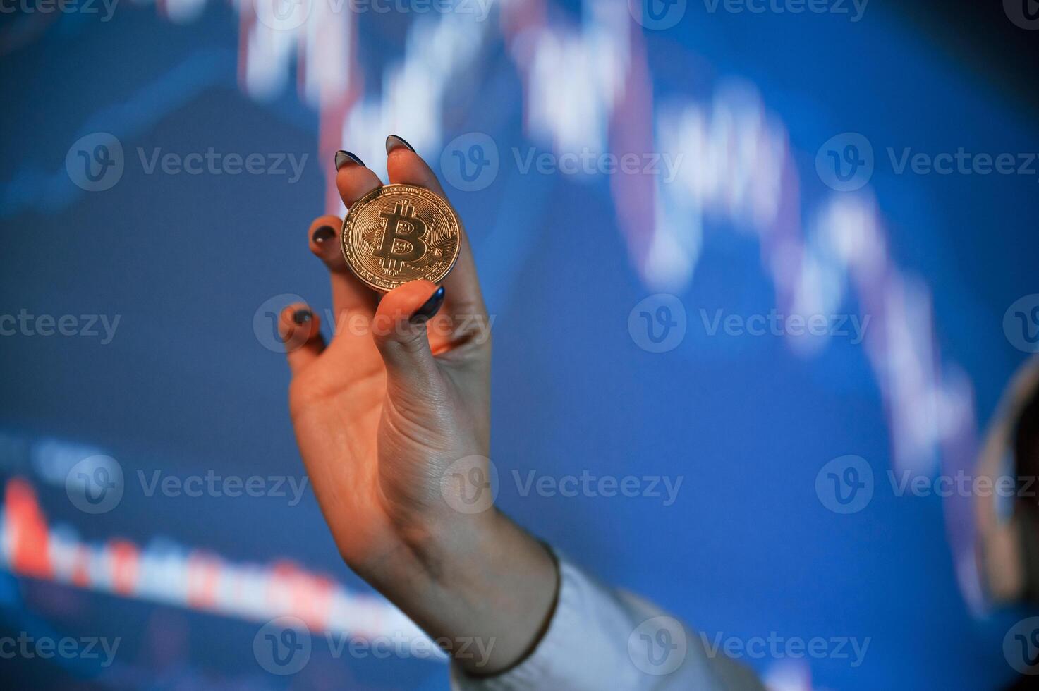 Close up view of woman's hand that holding ,physical bitcoin against background with graphs photo