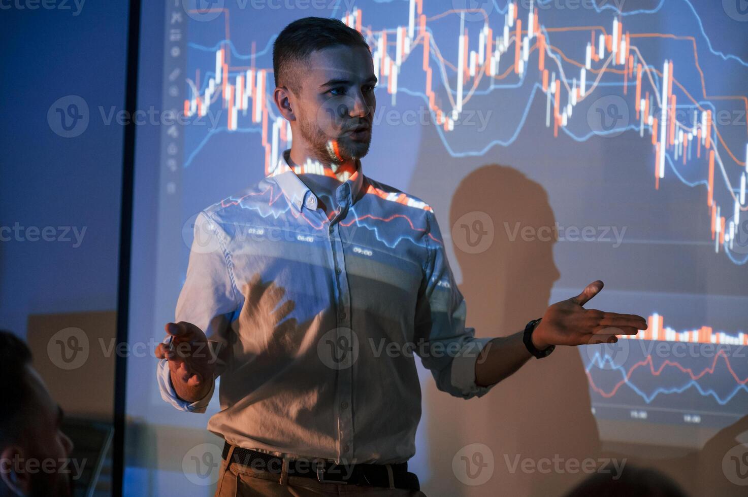 Man i,s standing near projector and showing graphs and business graphs photo
