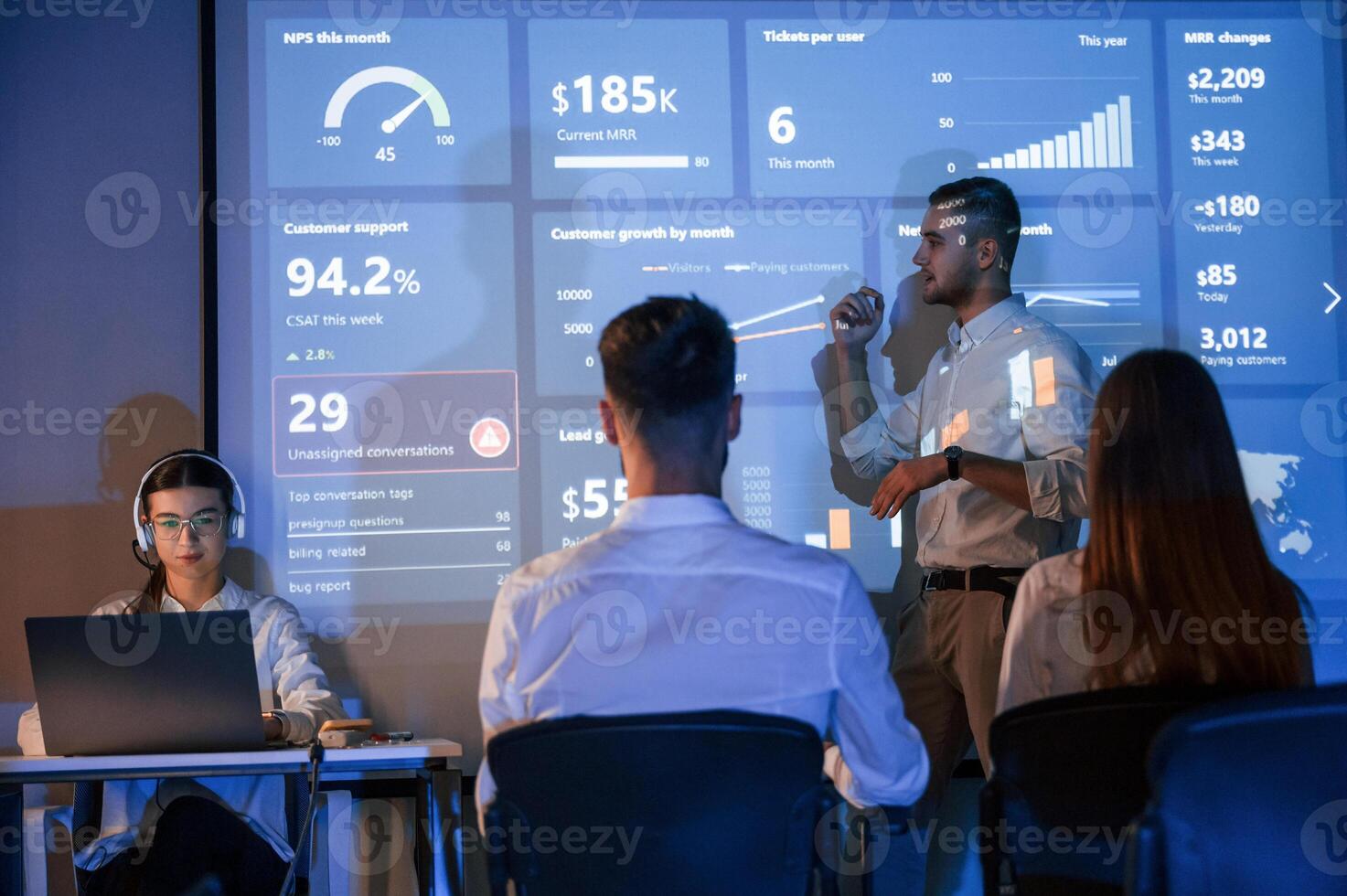 People,, are sitting. Male leader talking to employees, showing the plan on the projector in office of stock exchange company photo