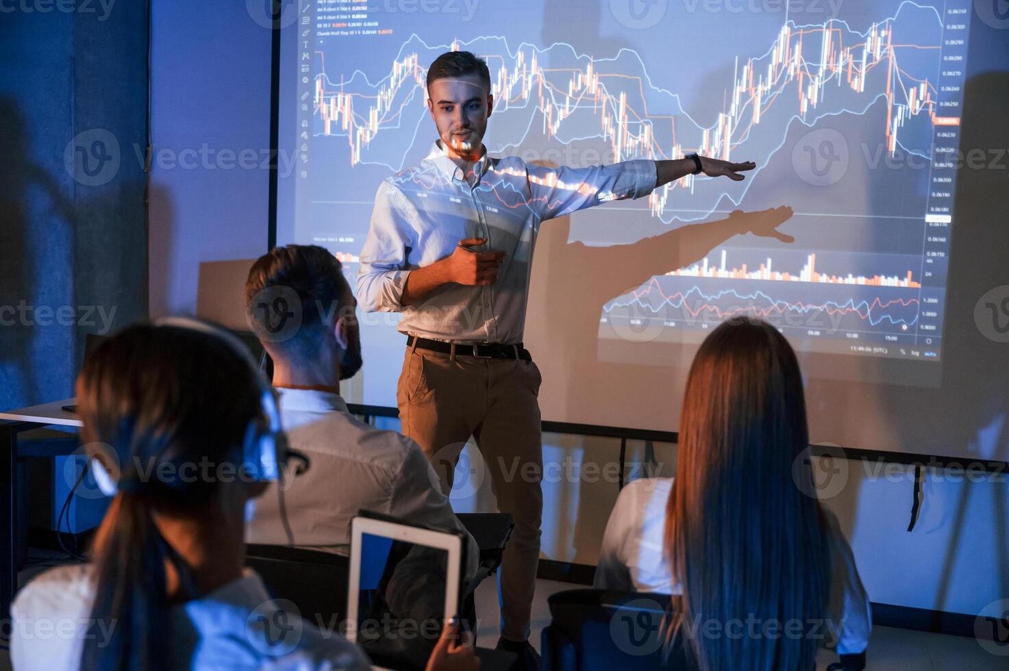 Showing information, by the hand. Male leader talking to employees, the projector in office of stock exchange company photo