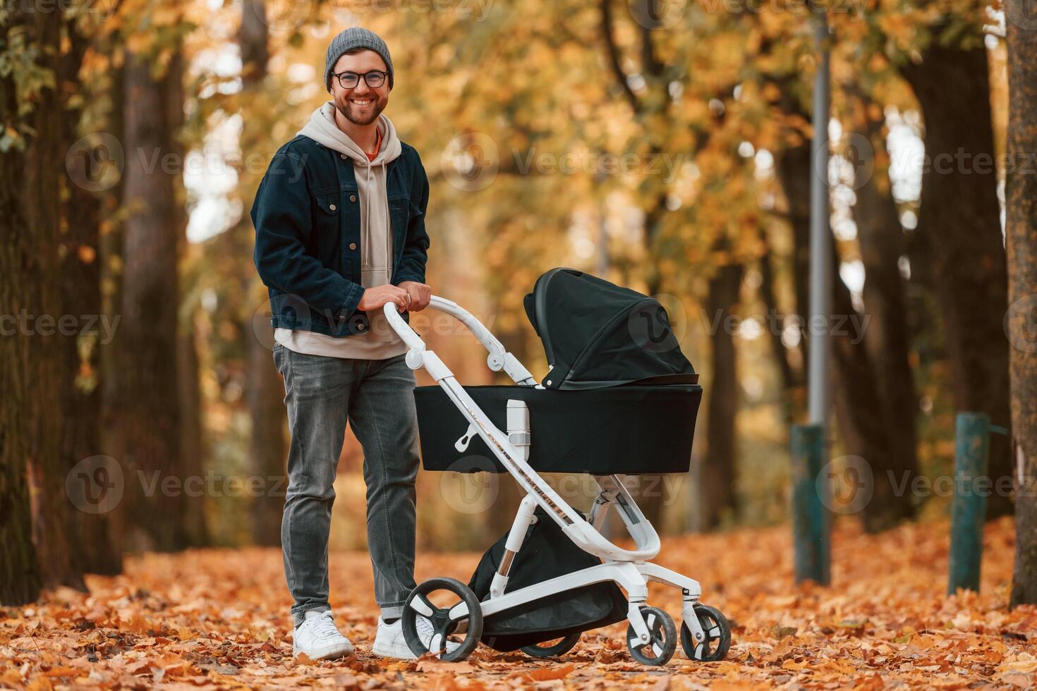 Standing and enjoying a nature. Man with pram, is having a walk in the autumn park photo