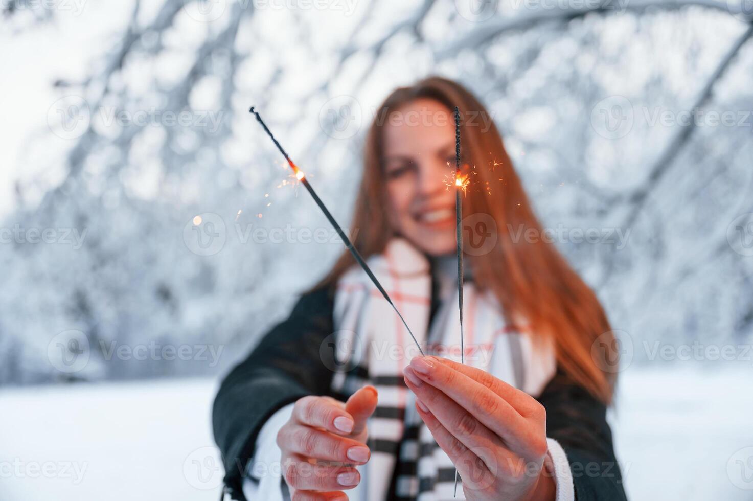 Holding, new year sparklers. Beautiful young woman is outdoors in the winter forest photo
