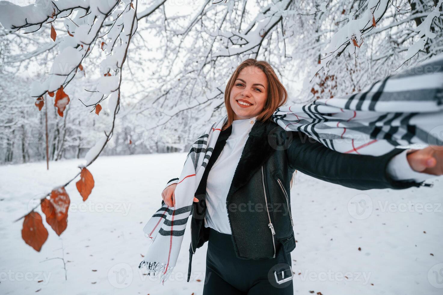Standing and, having fun. In warm scarf. Beautiful young woman is outdoors in the winter forest photo