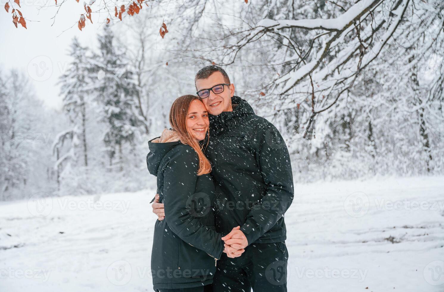 Standing and posing while embracing ,each other. Couple is in the winter forest, having a walk photo