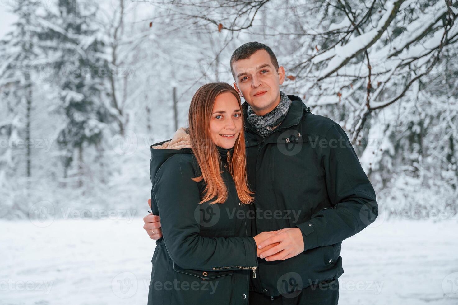 Standing and posing while embracing each other. Couple is in the winter forest, having a walk photo