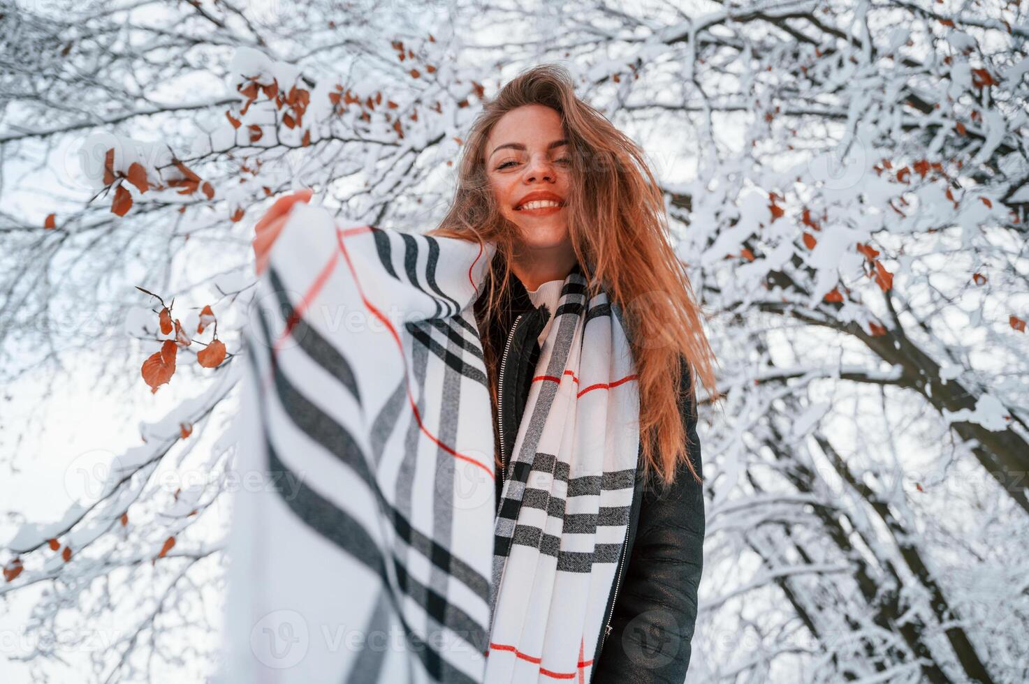 Standing, and having, fun. In warm scarf. Beautiful young woman is outdoors in the winter forest photo