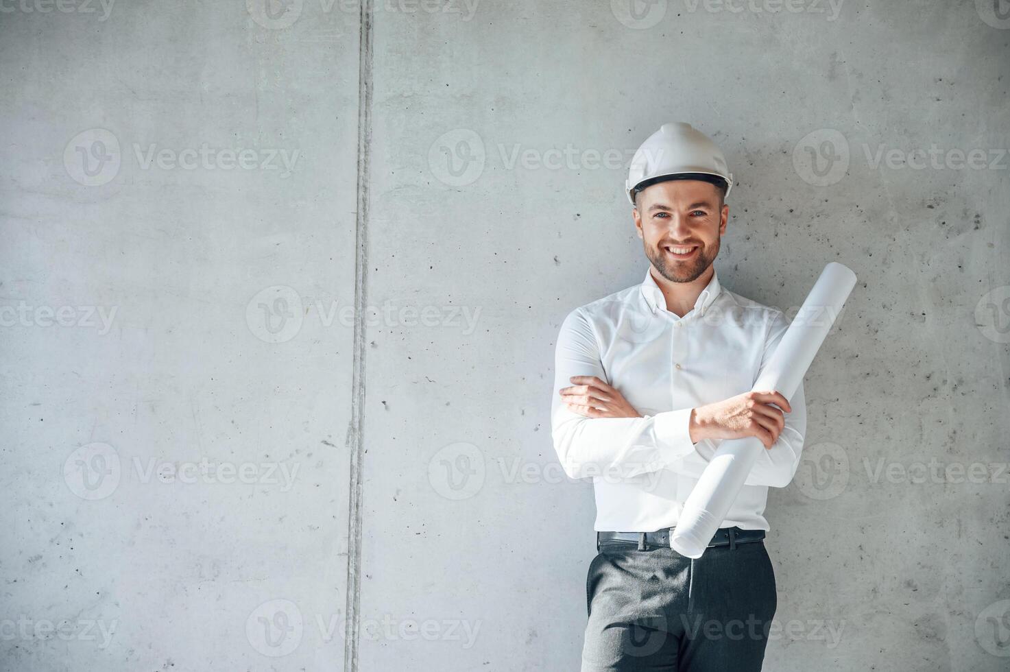 Leaning on the wall.. Holding paper with project plan. Man is working on the construction site at daytime photo