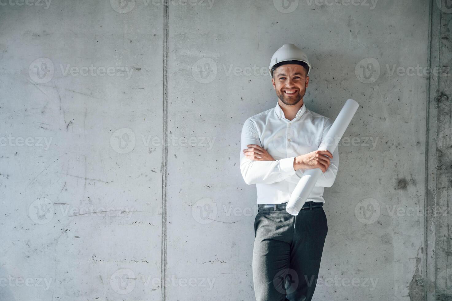Leaning ,on, the wall. Holding paper with project plan. Man is working on the construction site at daytime photo