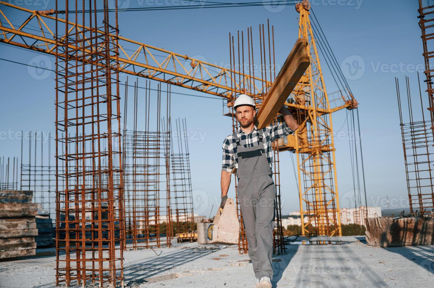 Crane behind.. Holding wooden ,piece. Man is working on the construction site at daytime photo
