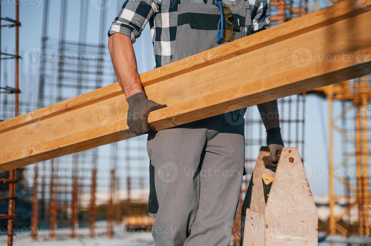 With ,big wooden plank in hand. Man is working on the construction site at daytime photo