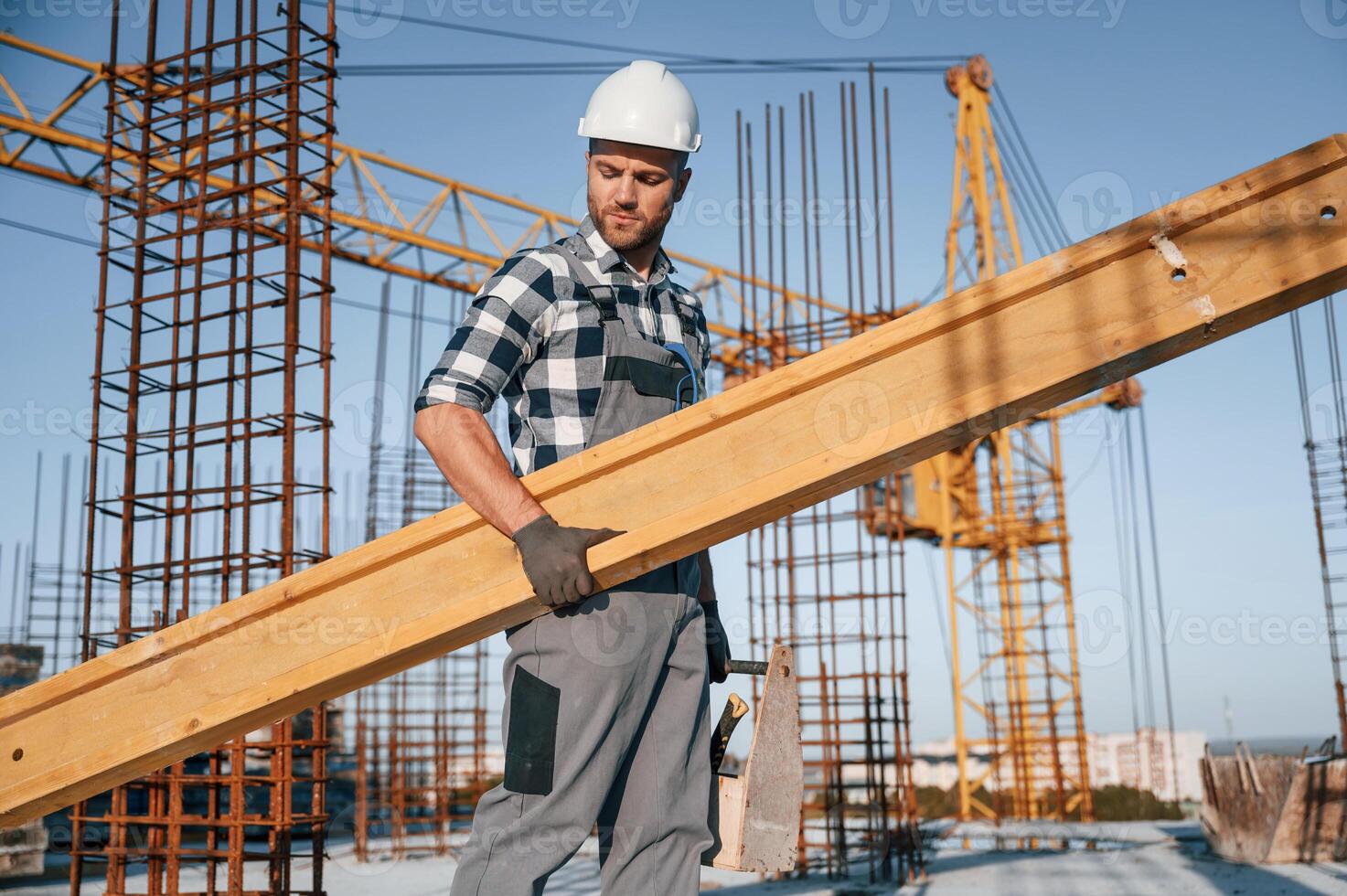 With big wooden ,plank, in hand. Man is working on the construction site at daytime photo