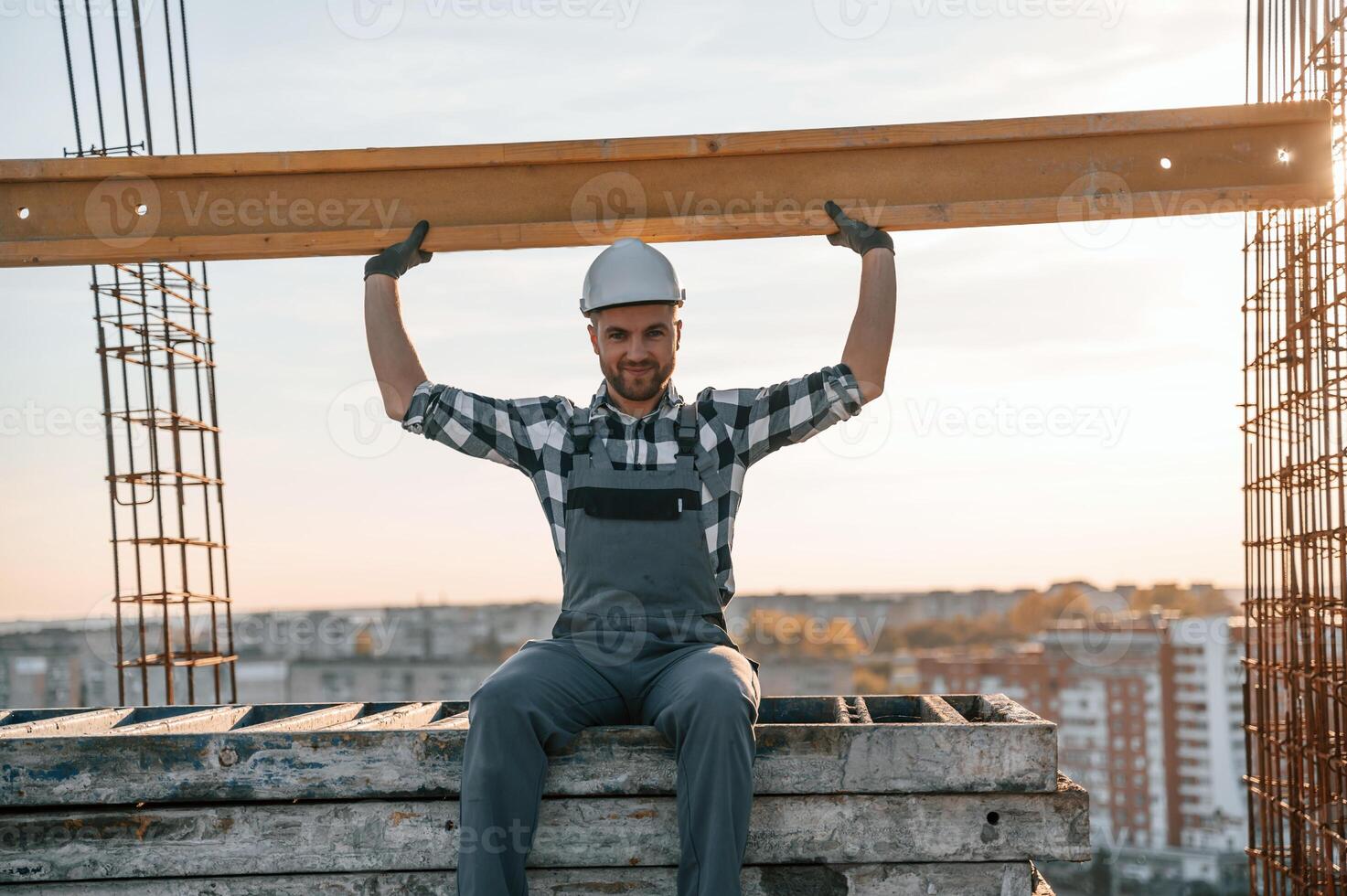 Sitting and holding wooden plank. Man is working on the construction site at daytime photo