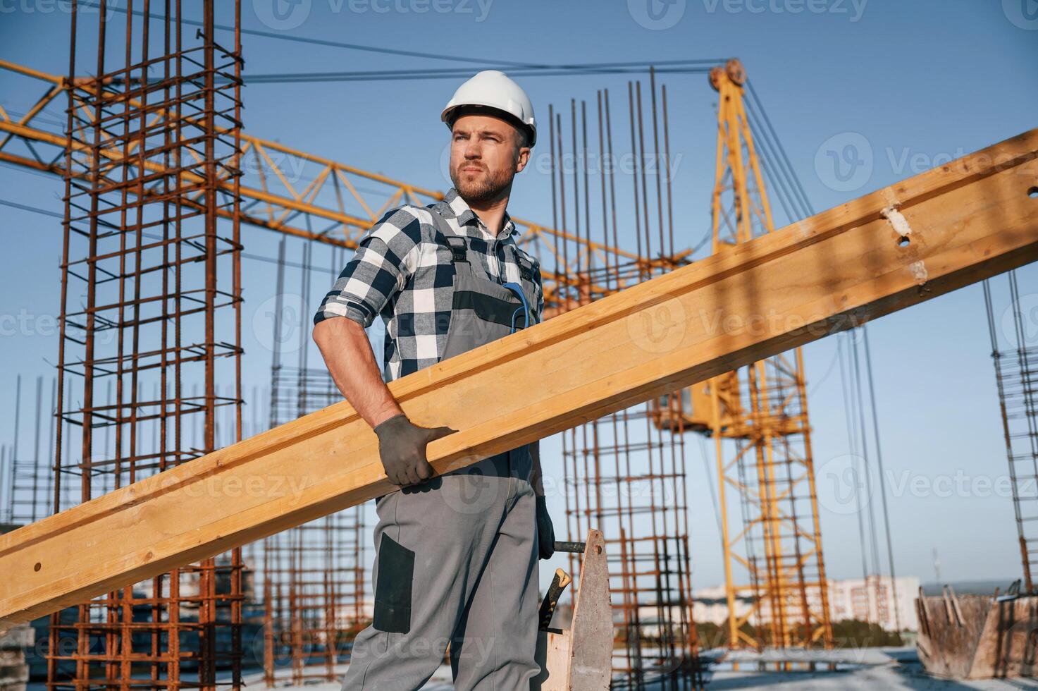With big wooden plank in hand. Man is working on the construction site at daytime photo
