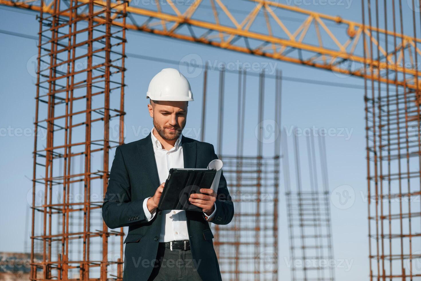 Standing and holding digital tablet. Businessman in formal clothes is on the construction site at daytime photo