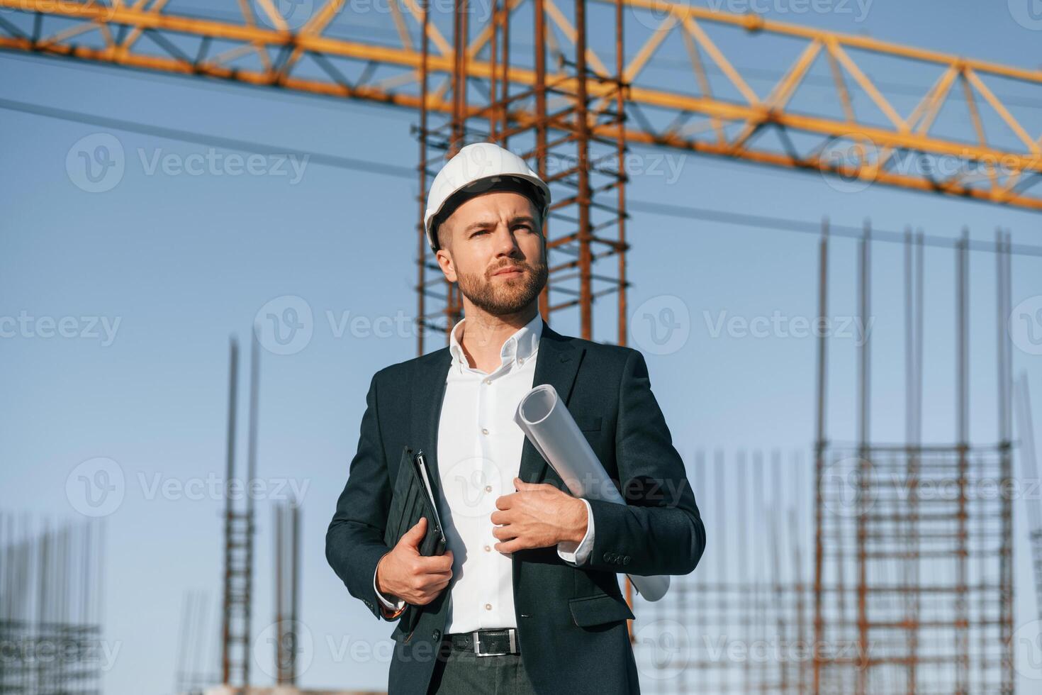 Holding paper with plan and tablet. Businessman in formal clothes is on the construction site at daytime photo