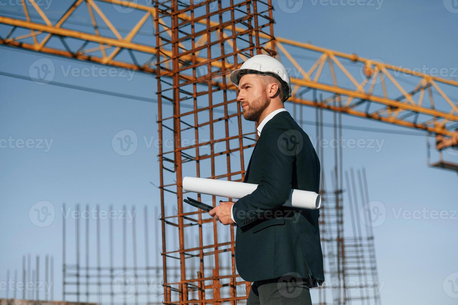 Side view. Walking and ,holding paper, with plan and digital tablet. Businessman in formal clothes is on the construction site photo